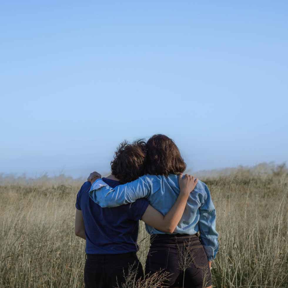 anonymous female friends embracing on spacious meadow
