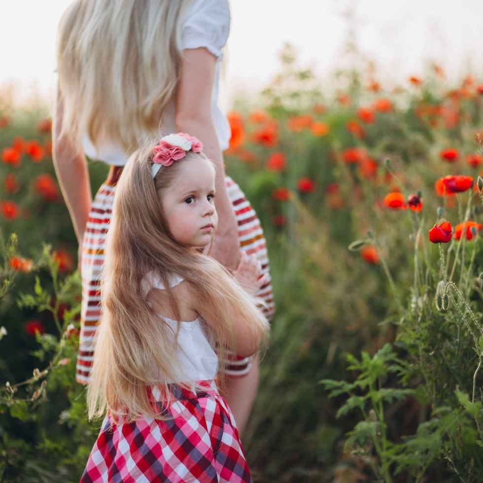 pensive little girl holding hand of mother in field